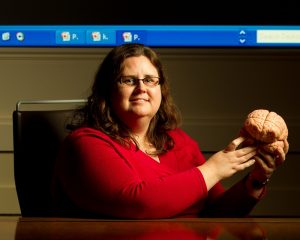 Dr. Kristen Kennedy seated at desk holding model of a brain. 